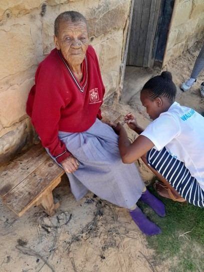 A nurse trims an older woman's nails during a home visit.