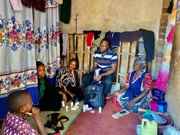 Family members and healthcare workers gather around an older woman receiving care at home.