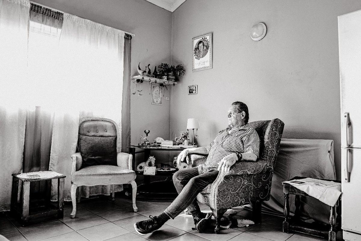 A widower receives continuing support, with an empty chair and his wife's portrait nearby.