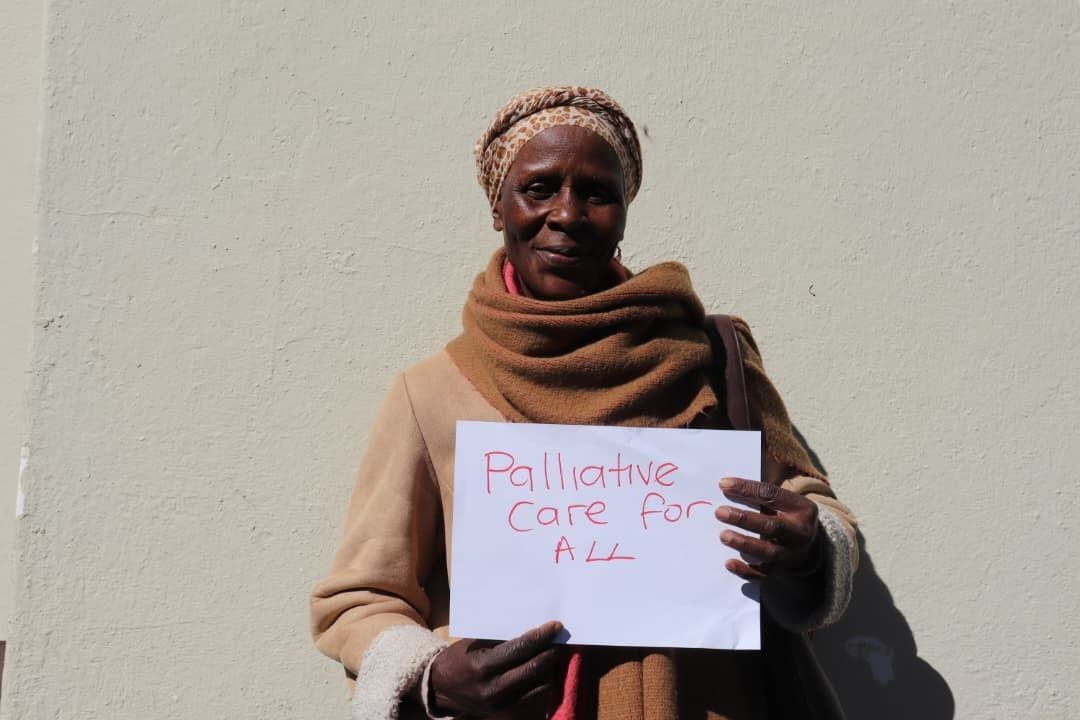 A participant shares her experience of care while holding a sign calling for palliative care for all.